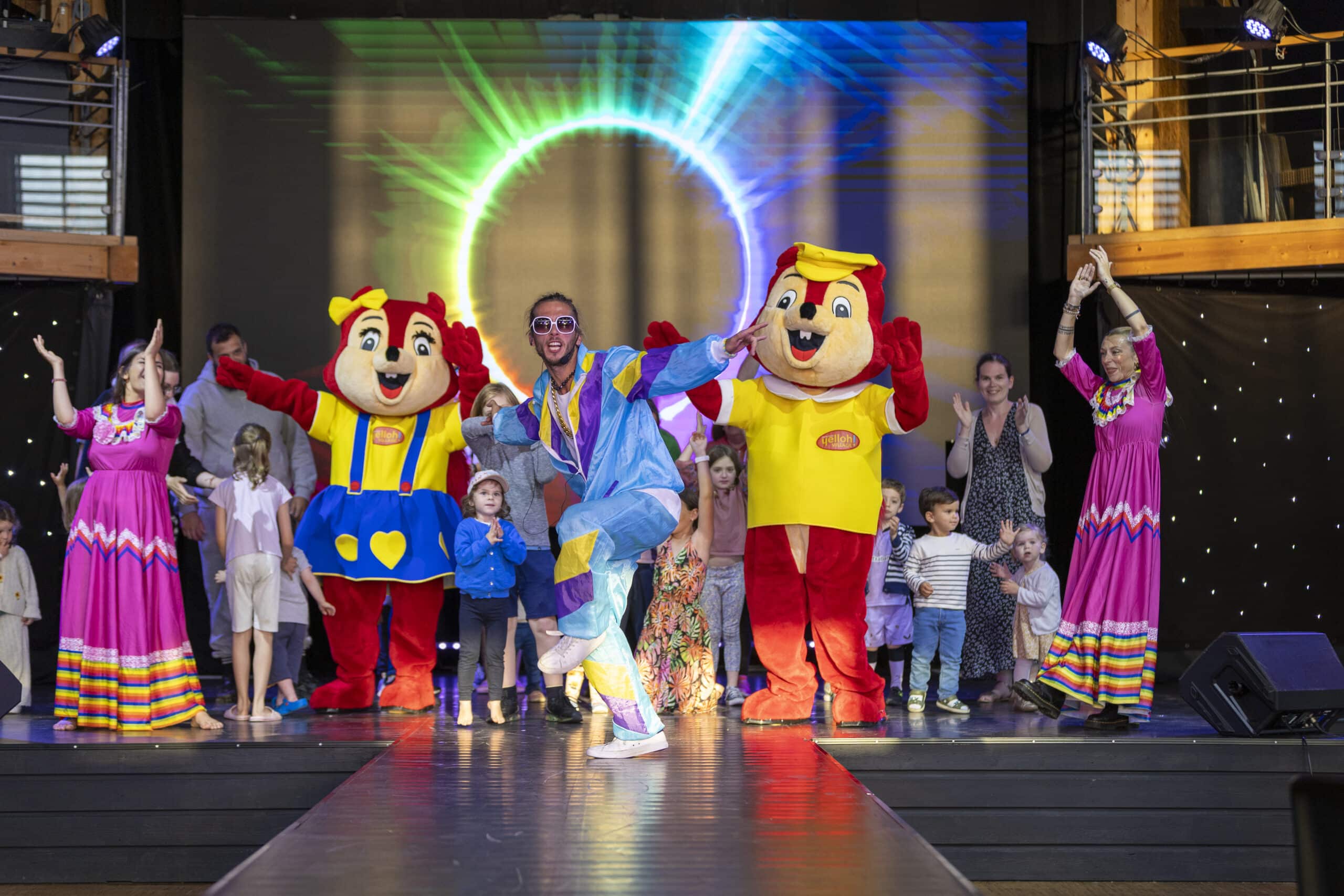 Spectacle coloré avec mascottes et enfants sur scène.